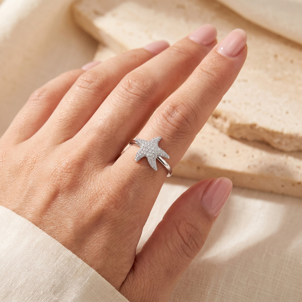 Angled view of a hand wearing a silver starfish ring with small pave-set clear stones.