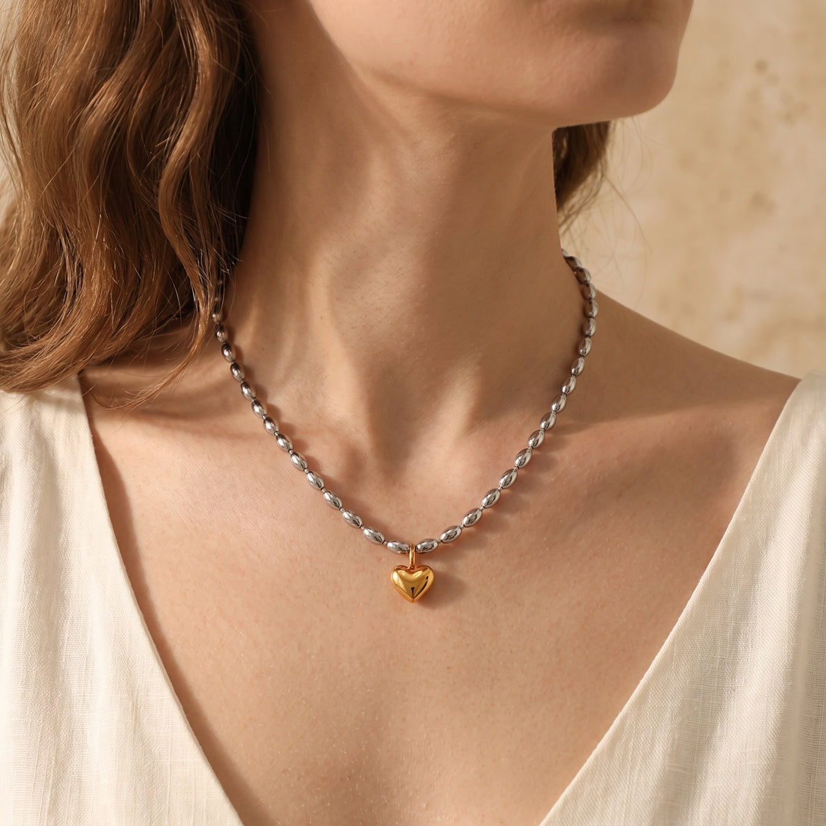 Front view of a model wearing the silver-tone bead necklace featuring a shiny gold-tone heart pendant.