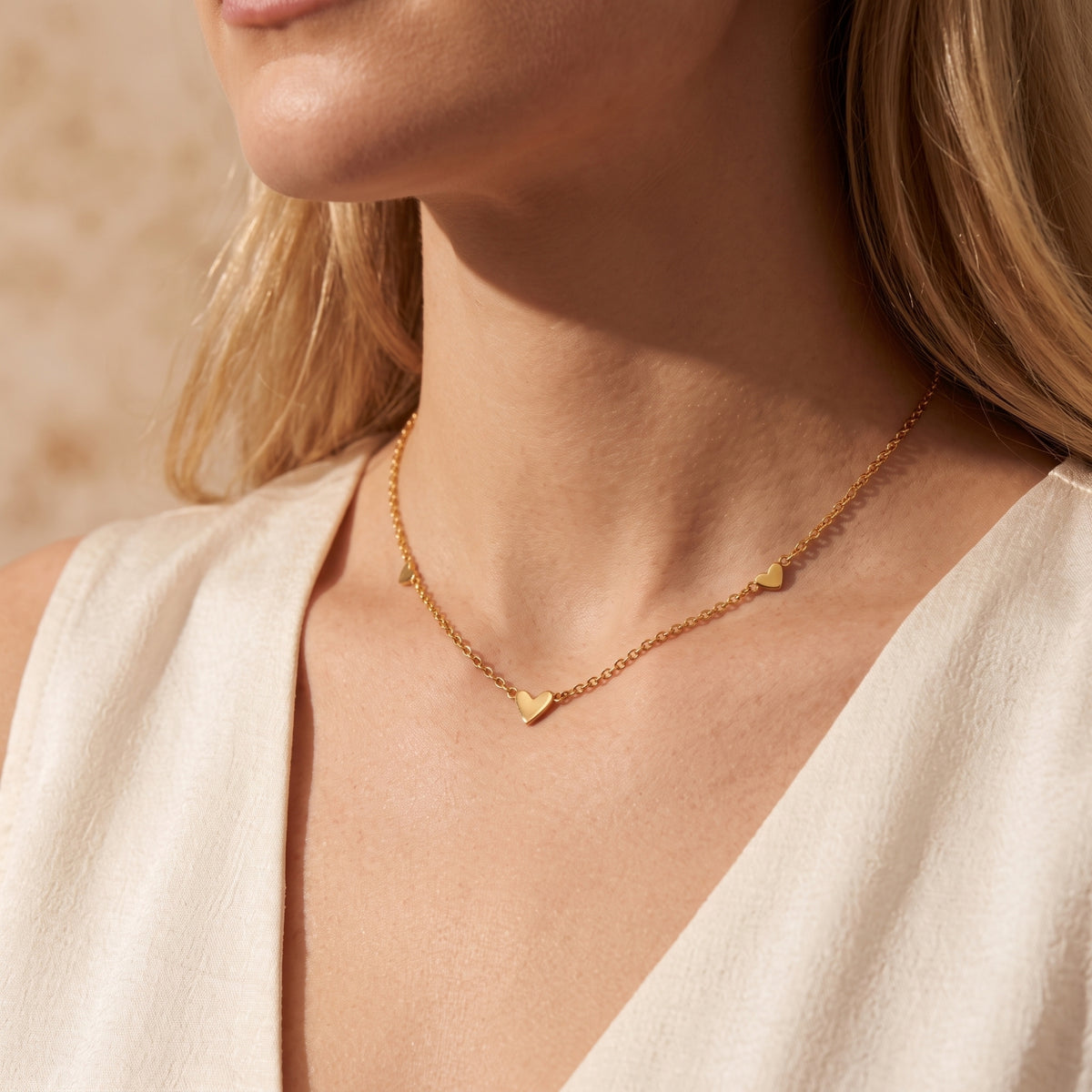Close-up of a model wearing the gold-tone heart station necklace with a cream V-neck top.