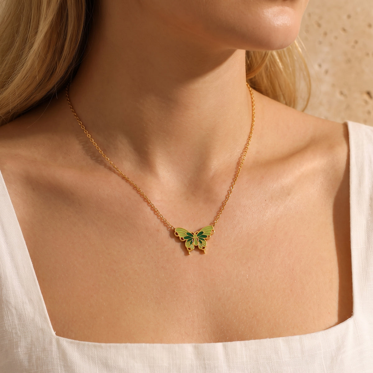Close view of a model wearing a gold-tone butterfly necklace with green and olive enamel and a white top.