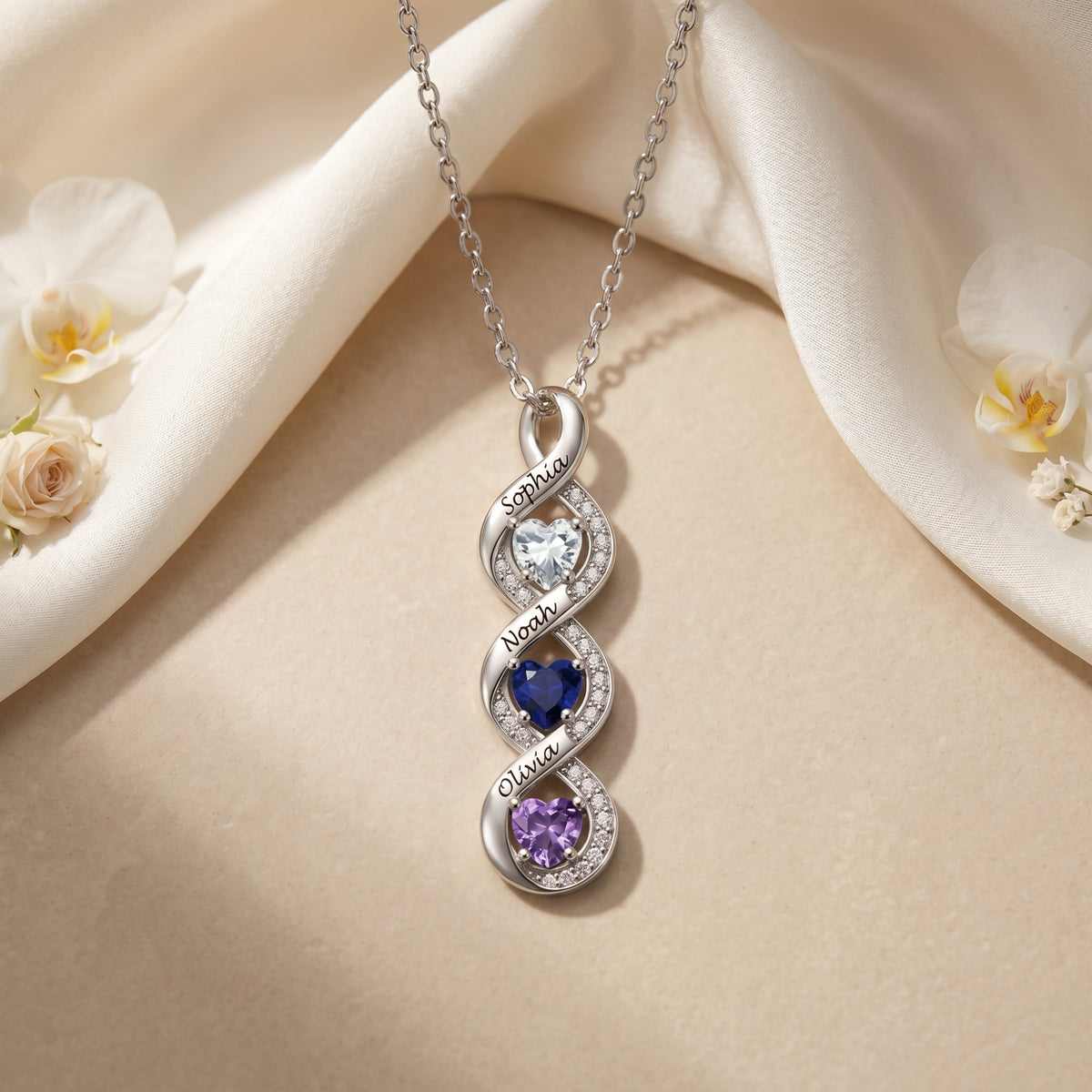 Silver infinity pendant necklace with three heart birthstones and engraved names on silk.