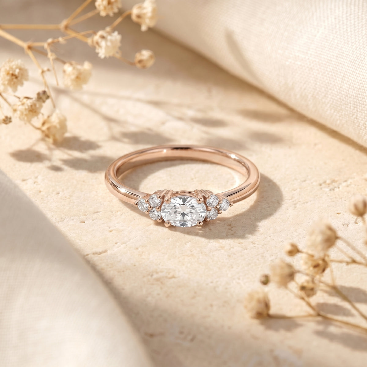 Rose gold oval cut moissanite ring displayed on a stone surface with floral accents.