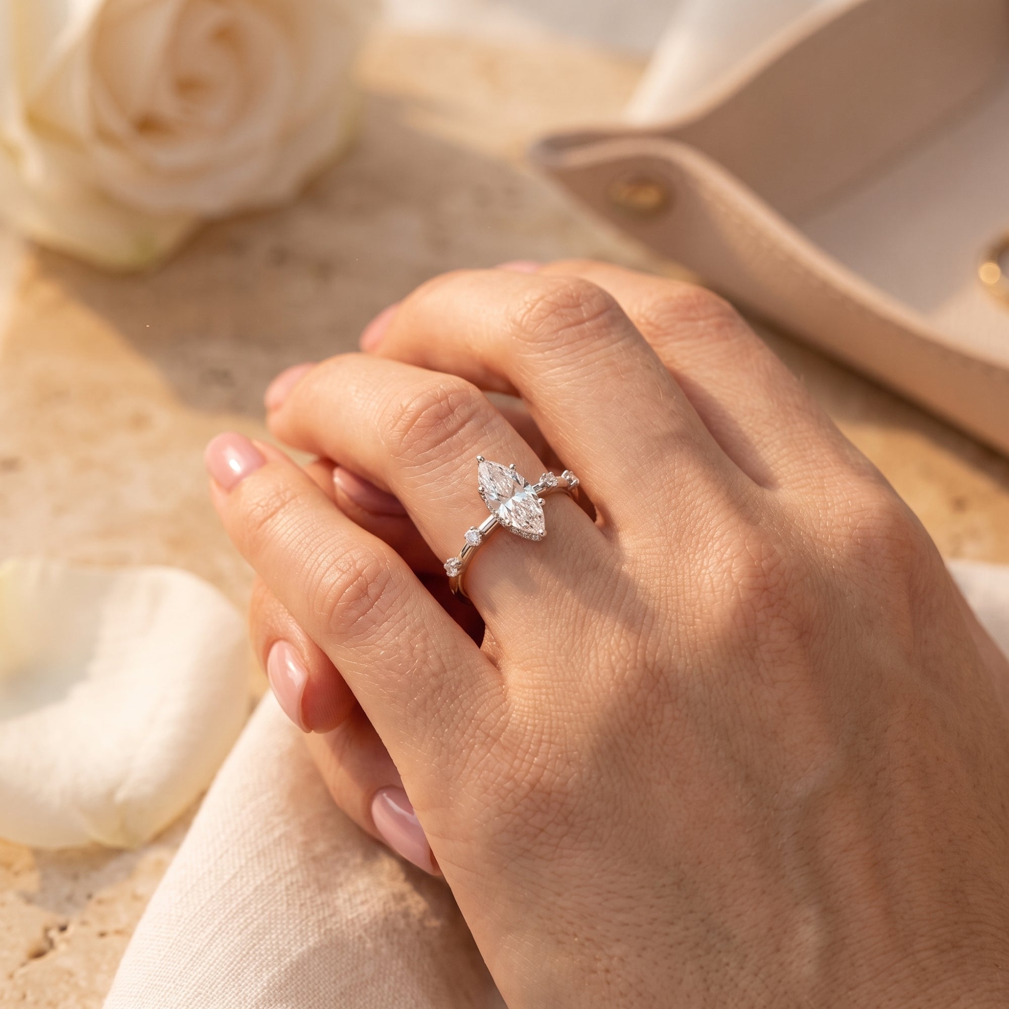 Sterling silver marquise cut simulated diamond ring worn on a hand with a white rose and tray in the background.