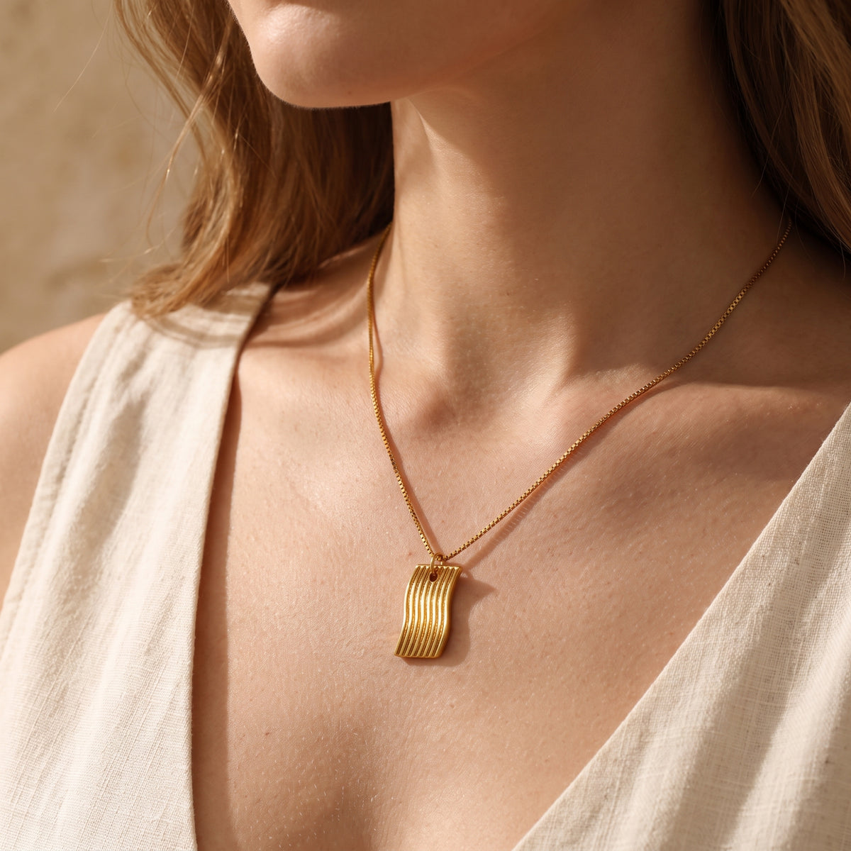 Model wearing the gold-tone wave pendant necklace, showcasing how it hangs against a cream top.