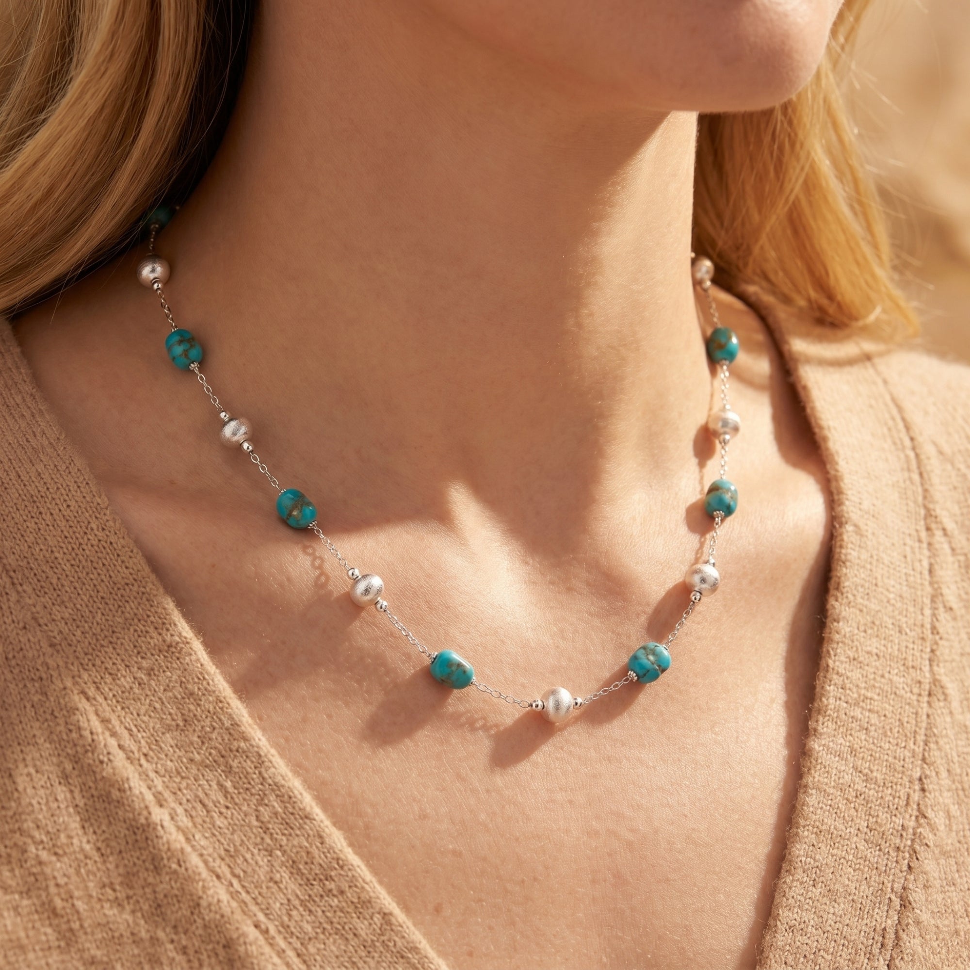 Close-up of turquoise and sterling silver necklace on a model wearing a tan sweater.