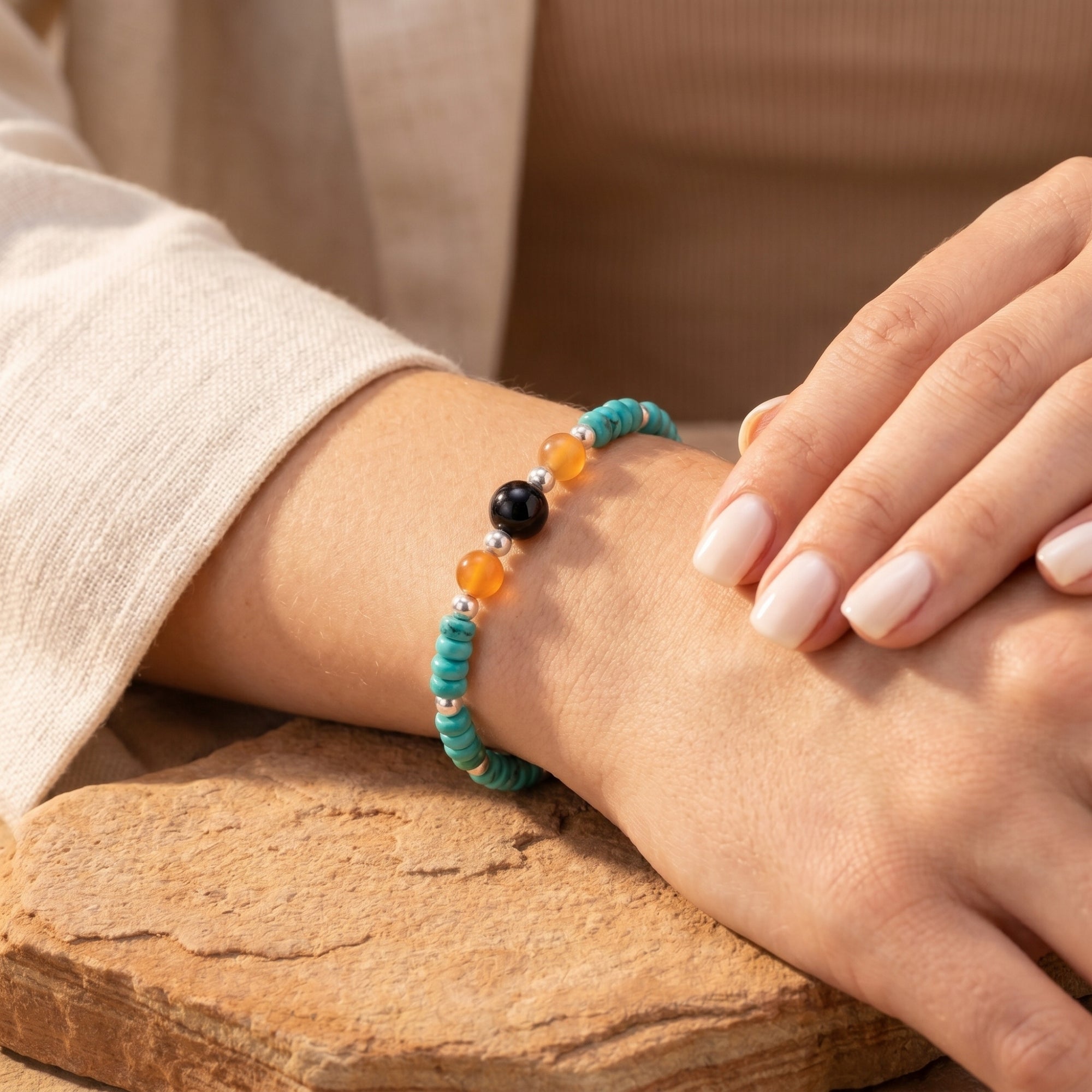 Close-up of the Desert Sky turquoise and carnelian bead bracelet on a model's wrist against a stone backdrop.