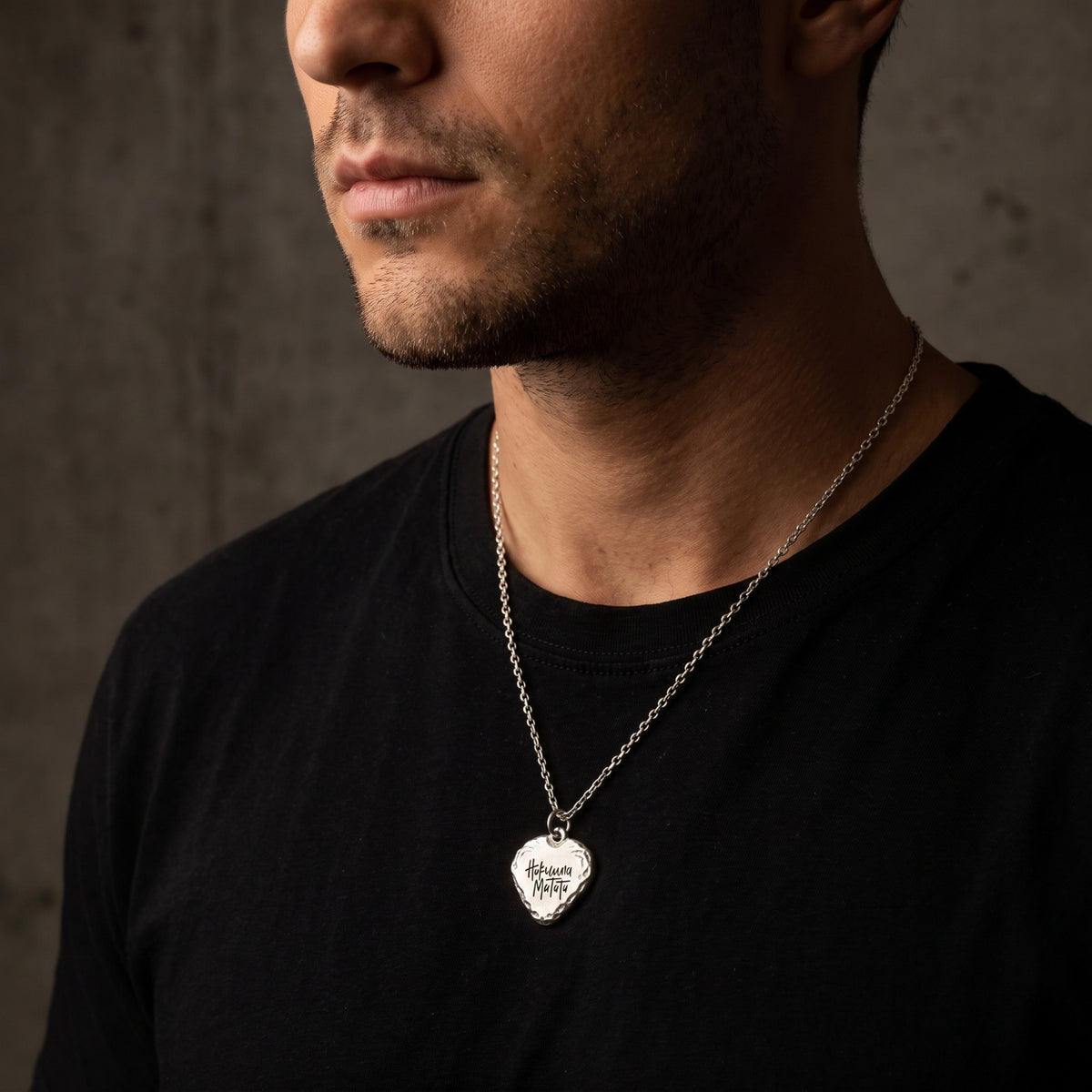 Three-quarter view of a man wearing the silver Hakuna Matata heart pendant necklace over a black T-shirt.