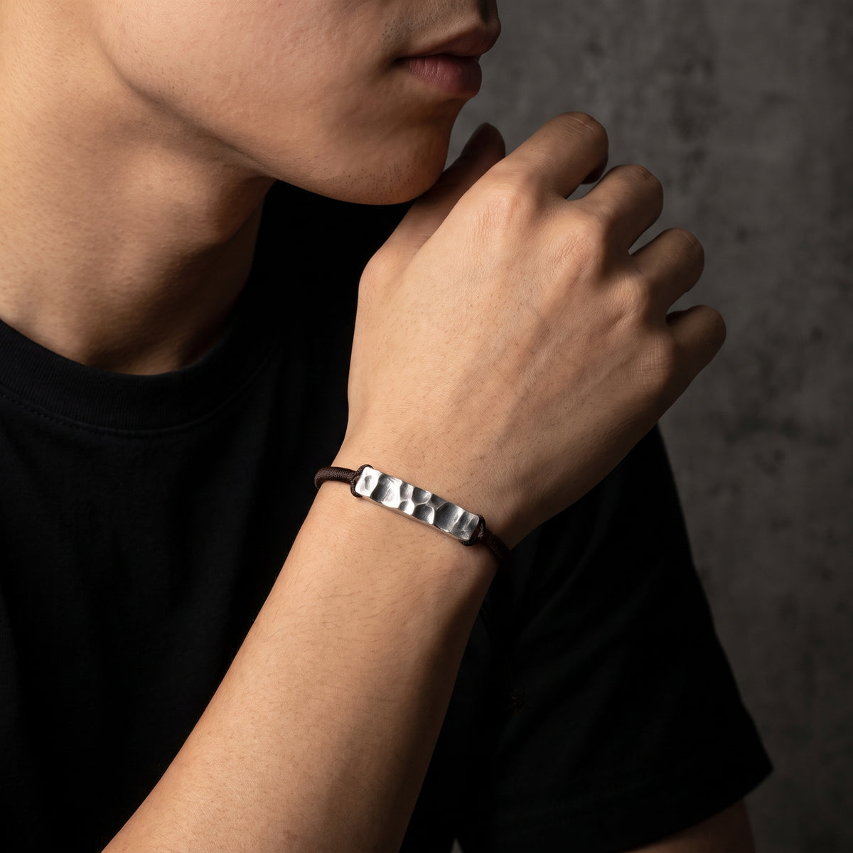 Close-up model view of the silver hammered bar cord bracelet worn on a man's wrist near his chin.