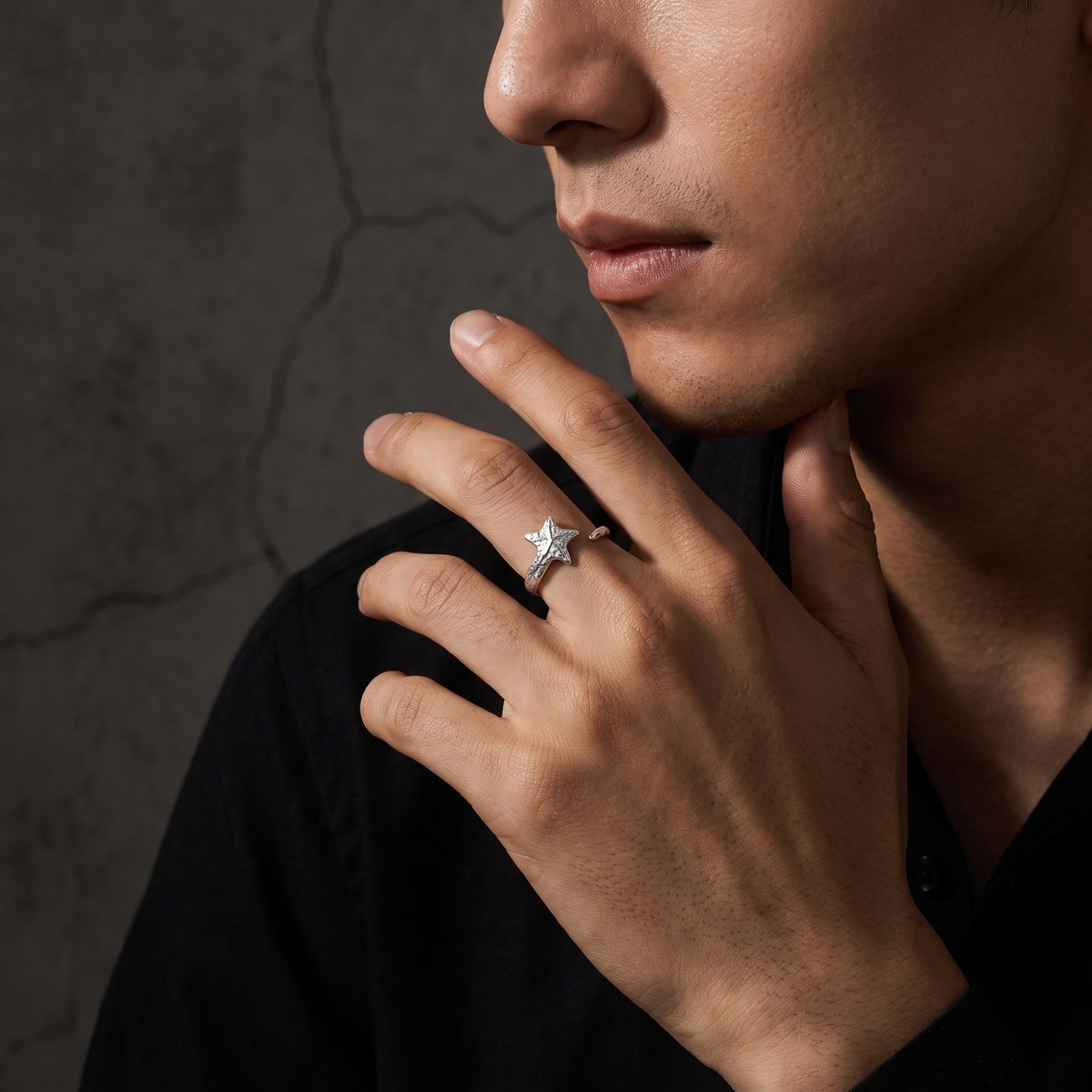 Side-profile view of a man wearing a textured silver star open ring against a dark background.
