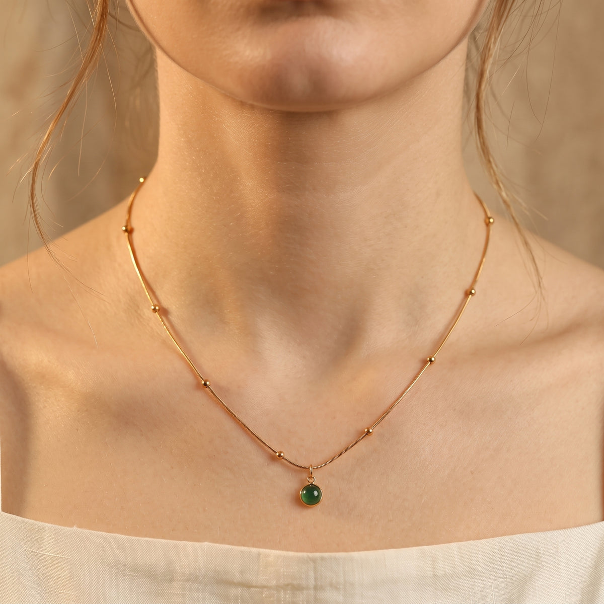 Front view of a model wearing the gold-tone station-bead necklace with a round green agate pendant over a white top.
