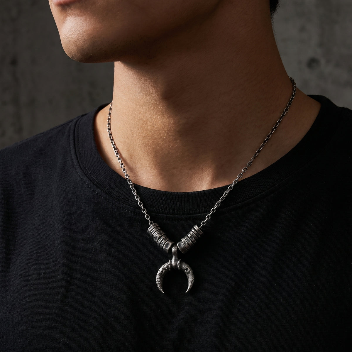 Cropped view of the crescent pendant necklace centered on a man's neck over a black shirt.