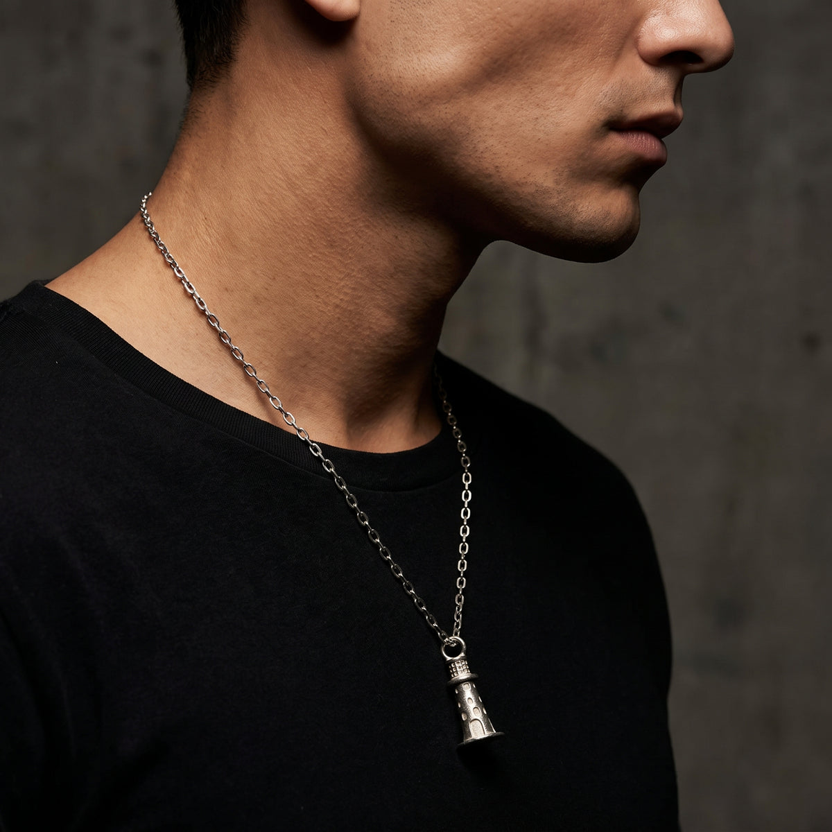 Side-profile view of a model wearing the silver lighthouse pendant necklace over a black T-shirt.