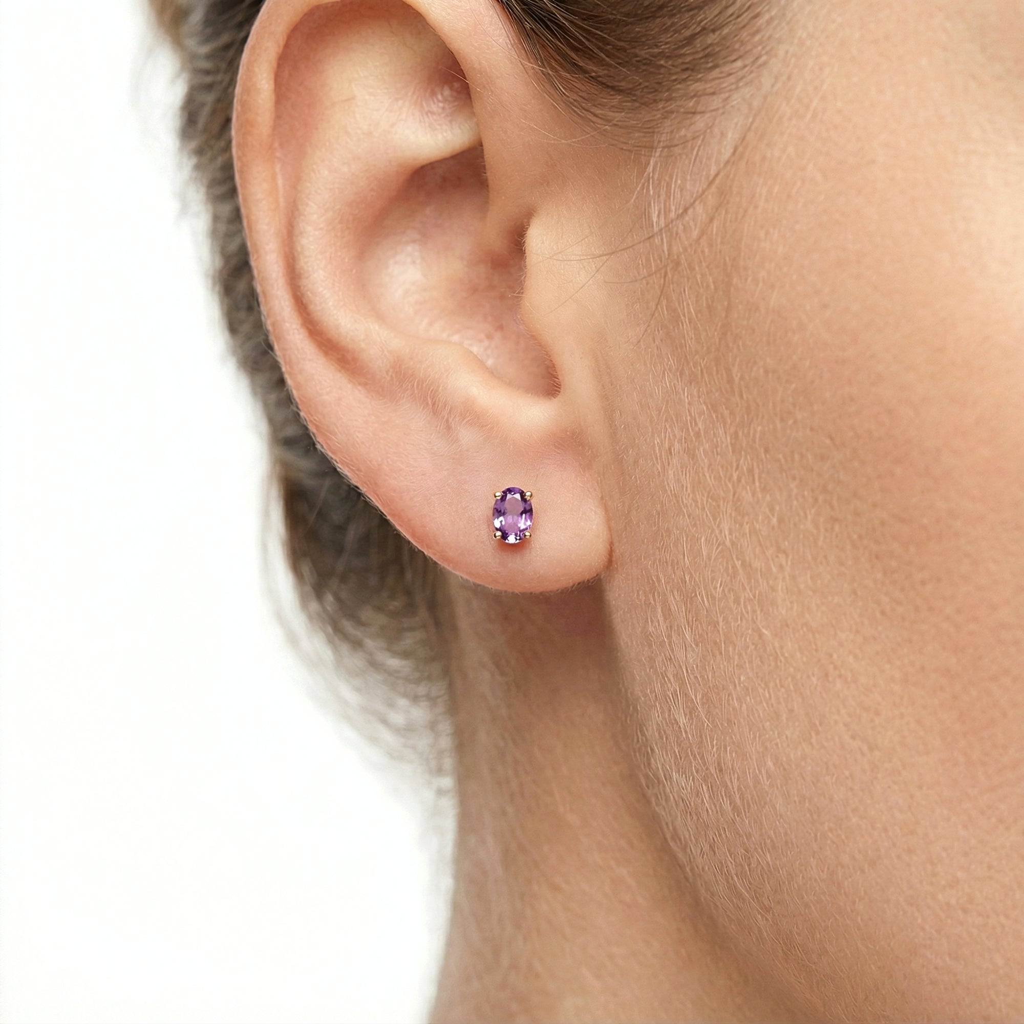 Close-up of an oval-cut simulated amethyst stud earring in 18K gold vermeil worn on an ear.