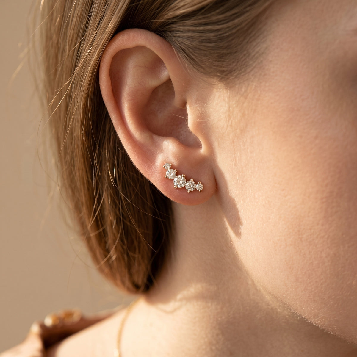 Close-up of gold moissanite climber earring on ear highlighting graduating stones.