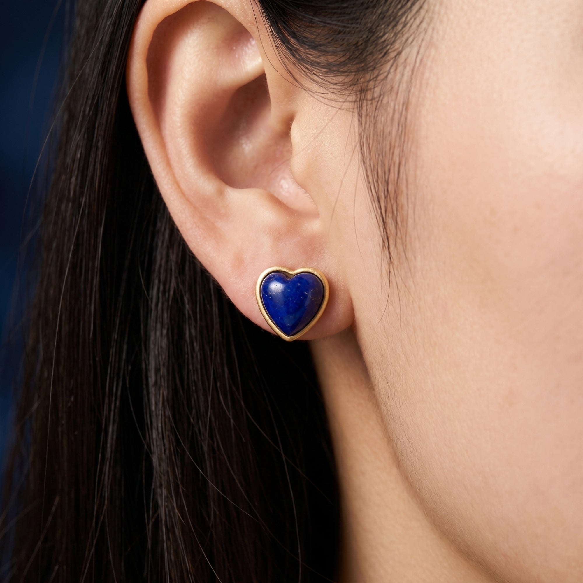 Close-up of a heart-shaped natural lapis lazuli cabochon stud earring in 18k gold plating on an ear.