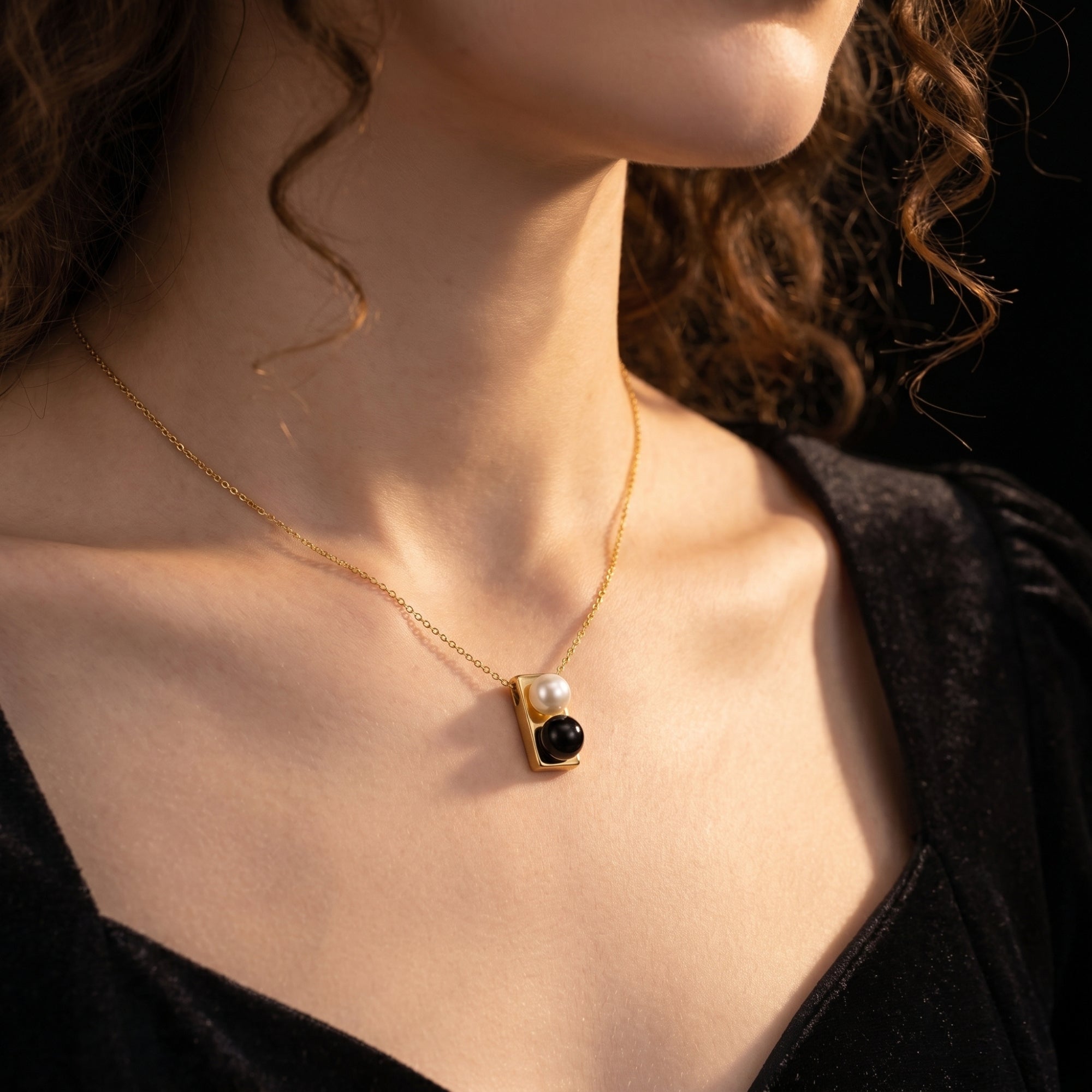 Model wearing the gold Equilibrium Onyx Necklace featuring a stacked pearl and black onyx pendant.