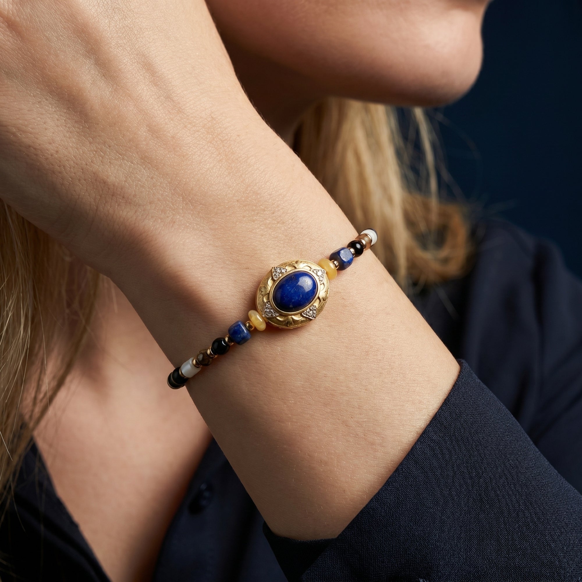 Macro view of the gold-plated oval charm and lapis lazuli beads on a woman's wrist.