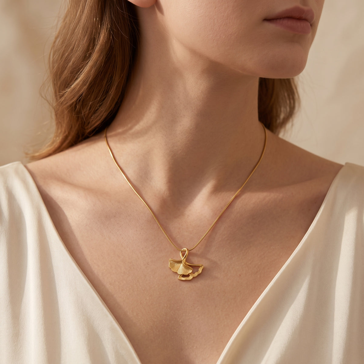 Centered front view of the gold-tone double ginkgo leaf pendant necklace worn against a model's neck.