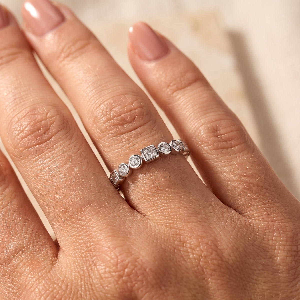 Silver promise ring with alternating princess and round-cut stones worn on a hand.
