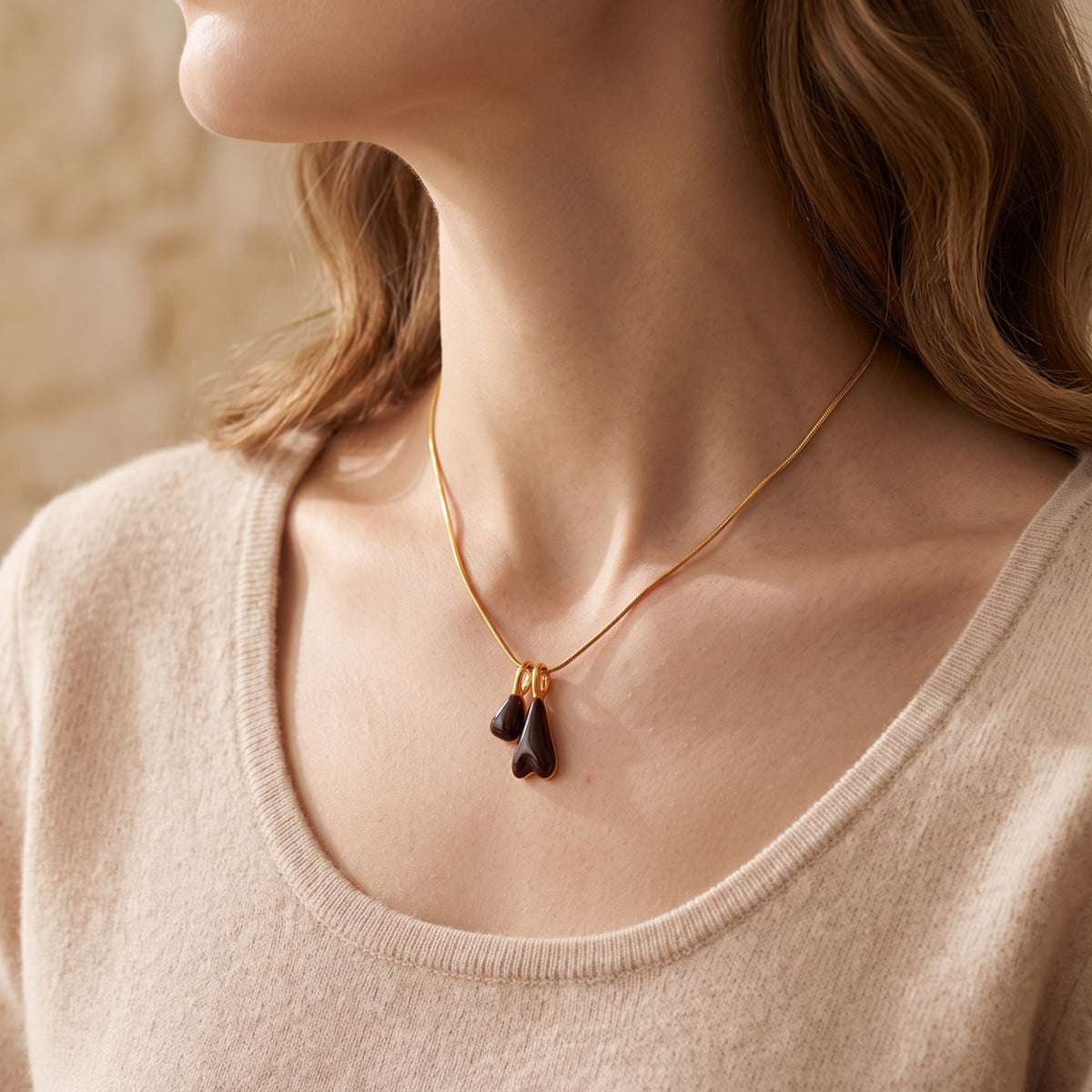 Marais gold stainless steel pendant necklace with burgundy drops worn by a model in a beige sweater.