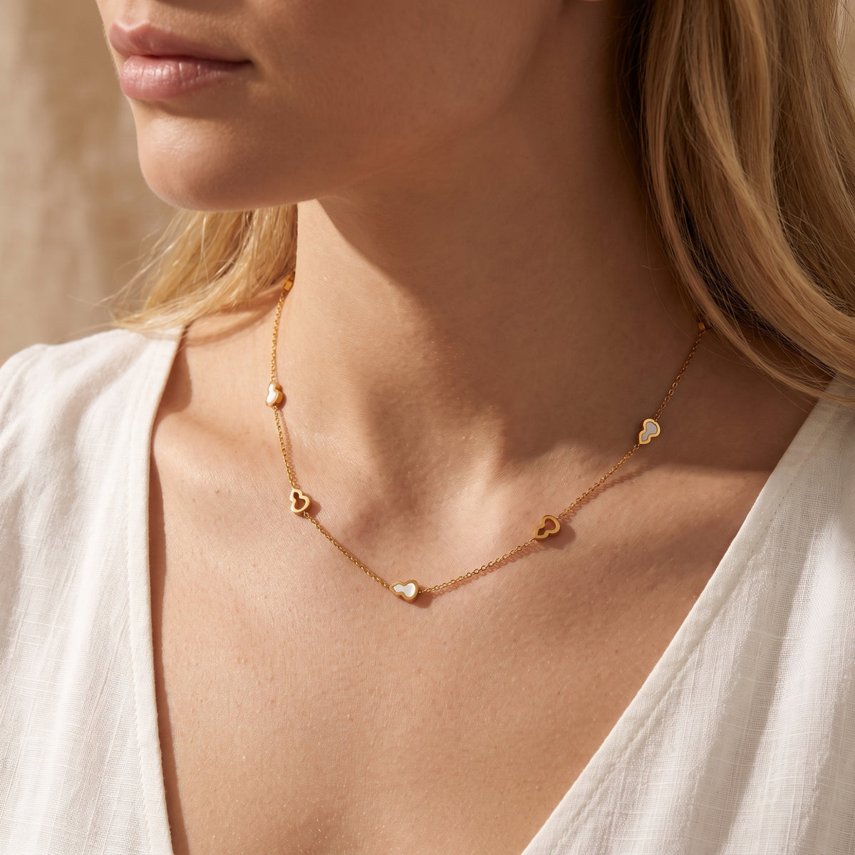 Close-up of a blonde model wearing the gold-tone station necklace with white inlay gourd motifs and a white open blouse.