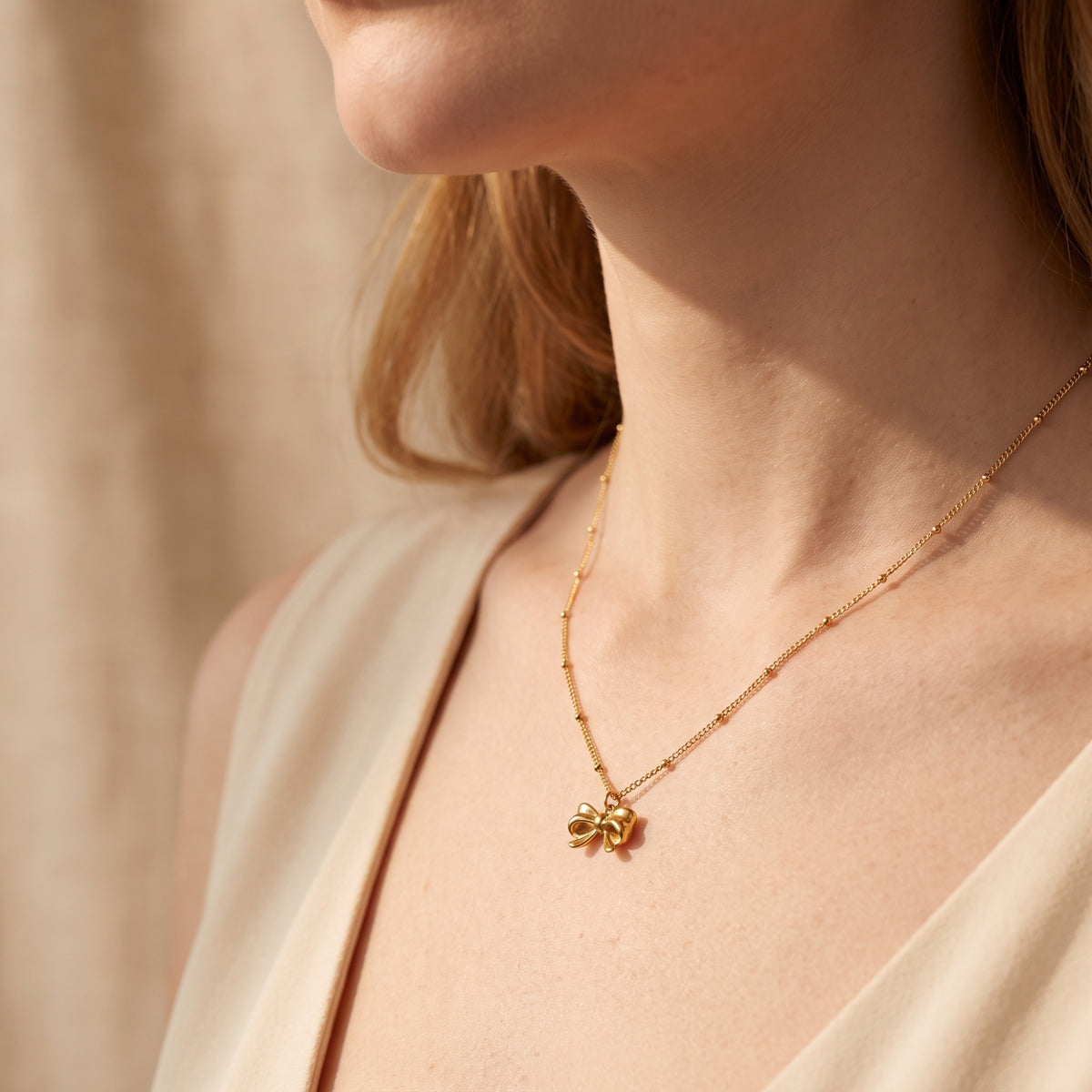 Side-angle view of a model wearing the gold-tone ribbon bow necklace with a beige V-neck top.