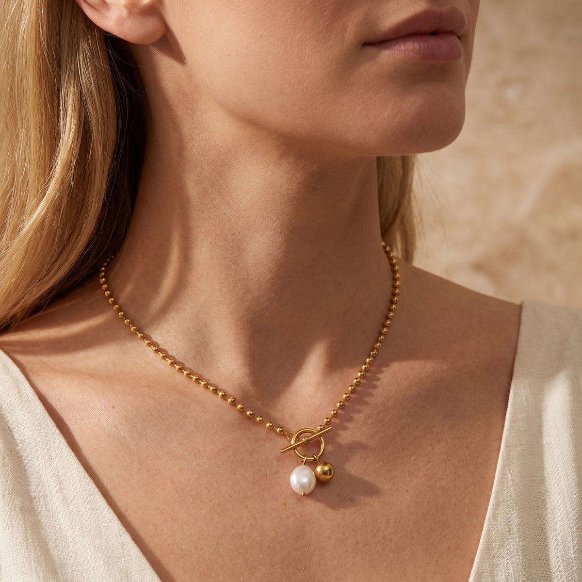 Close-up of a model wearing the gold-tone pearl toggle necklace with a light V-neck top.
