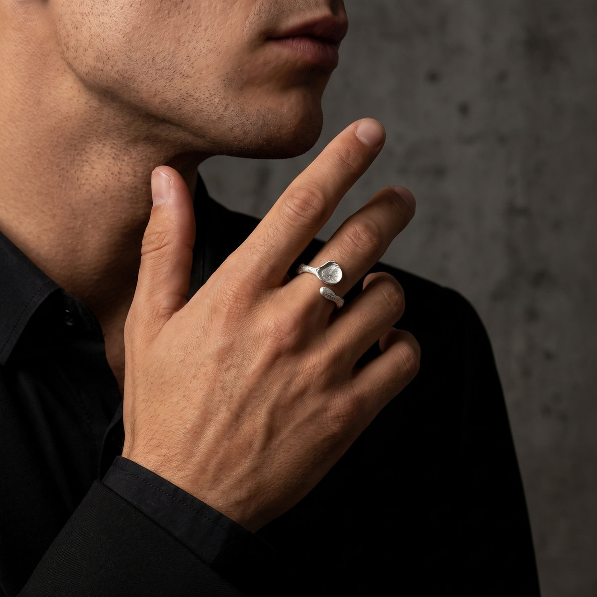Close-up of a man holding his hand near his chin while wearing the silver bark-textured open ring.