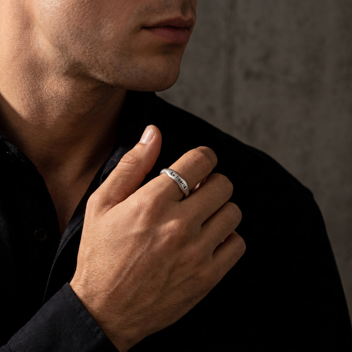 Man wearing the engraved open band ring on his index finger against a dark backdrop.