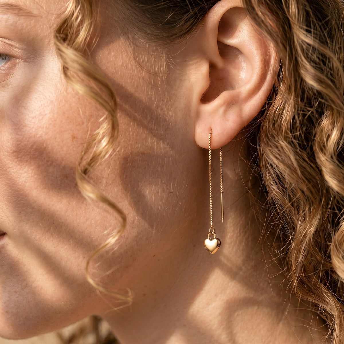 Side view of a model wearing a gold heart threader earring, highlighting the elegant drape of the box chain.