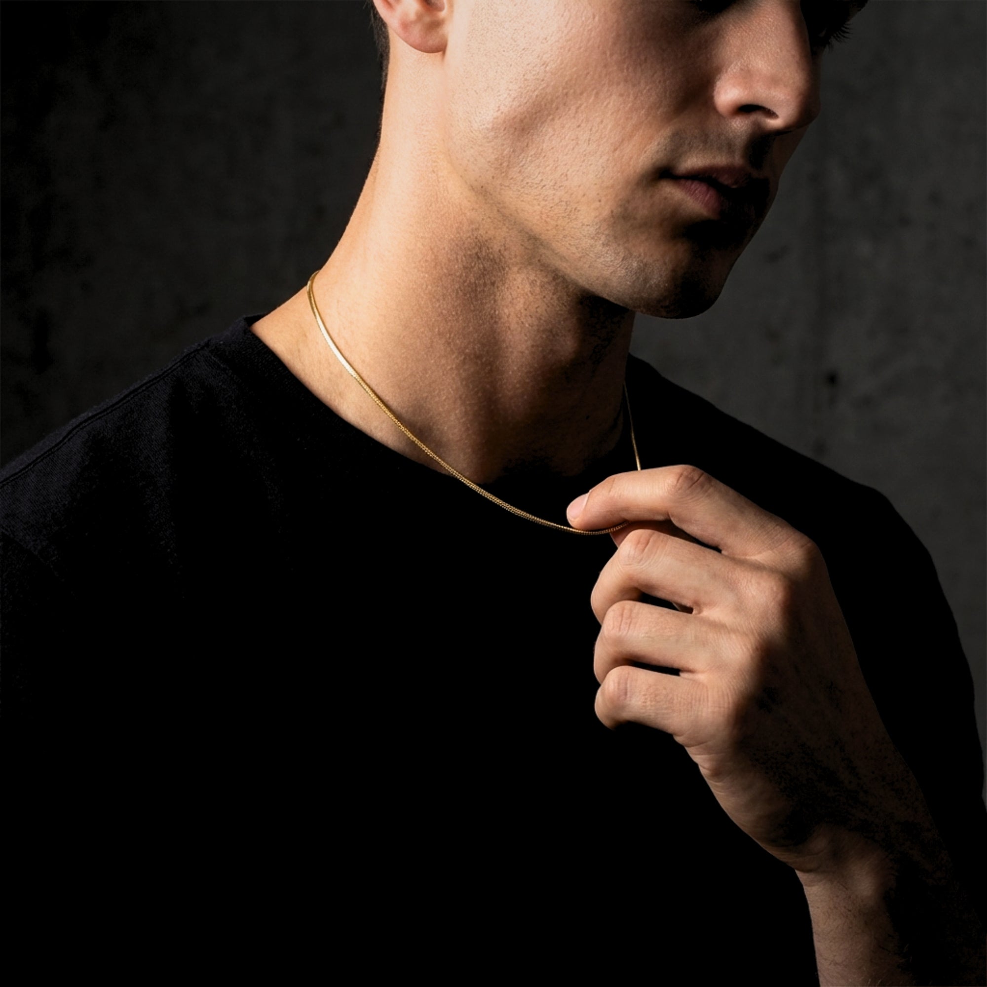 Close-up of a man's hand adjusting the gold stainless steel Square Dance Chain around his neck.