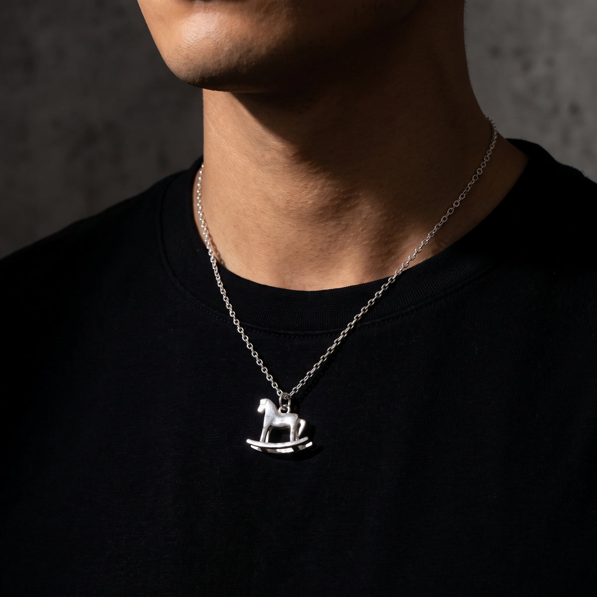 Front view of a model wearing the silver rocking horse pendant necklace over a black crewneck shirt.