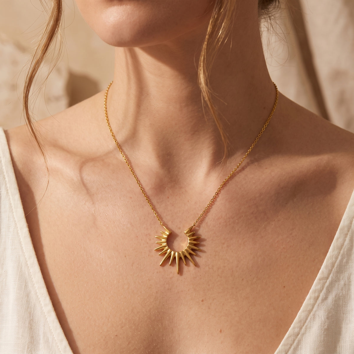 Centered view of a model wearing the gold-toned sunburst pendant necklace with a white v-neck top.