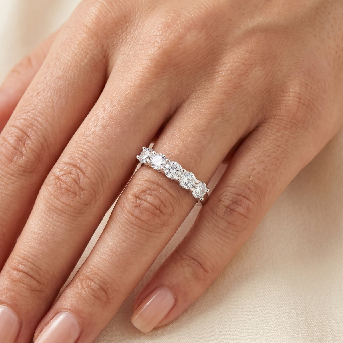 Close-up of a silver five-stone band set with round sparkling stones worn on a hand.