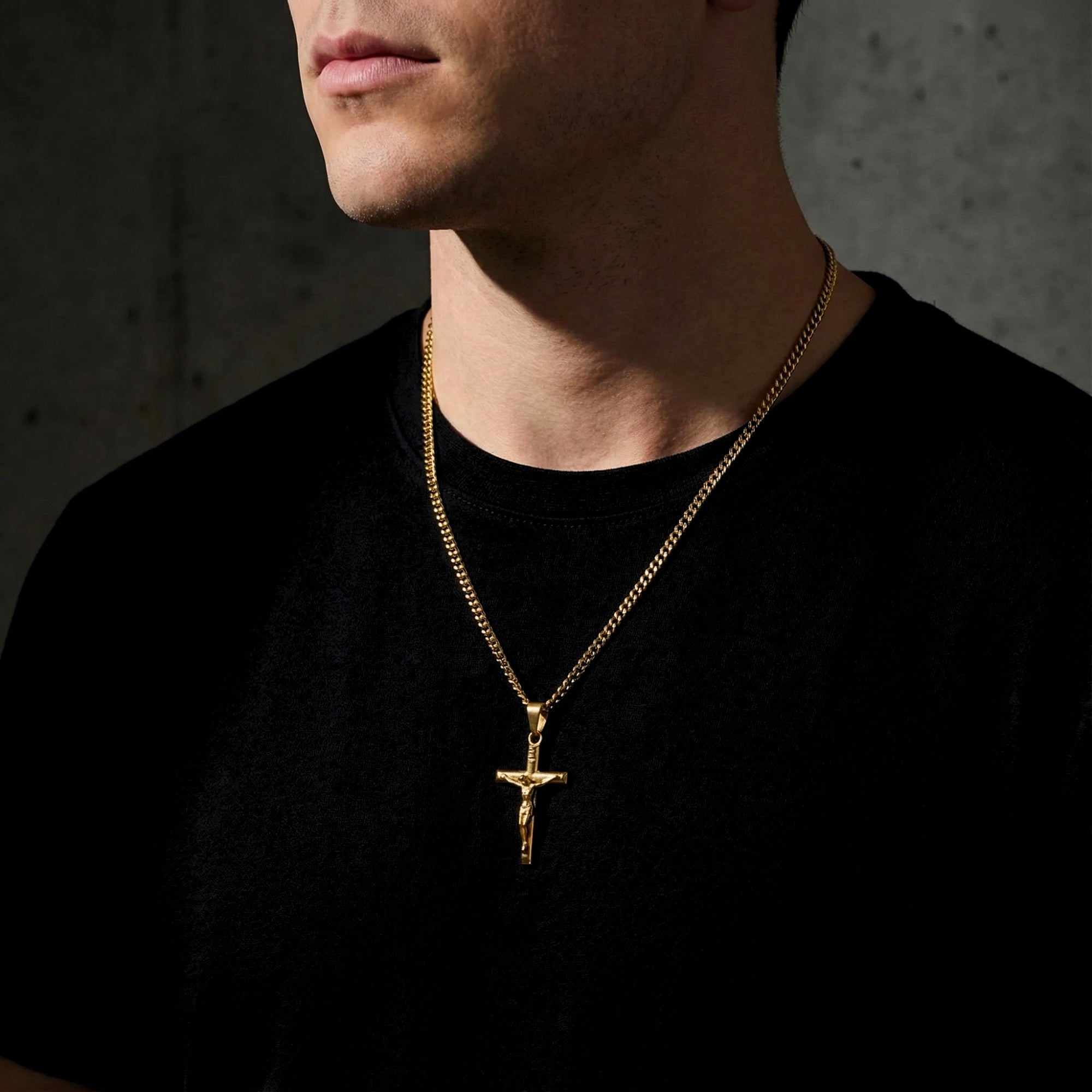 Side view of a man wearing the gold stainless steel crucifix pendant necklace over a black t-shirt.