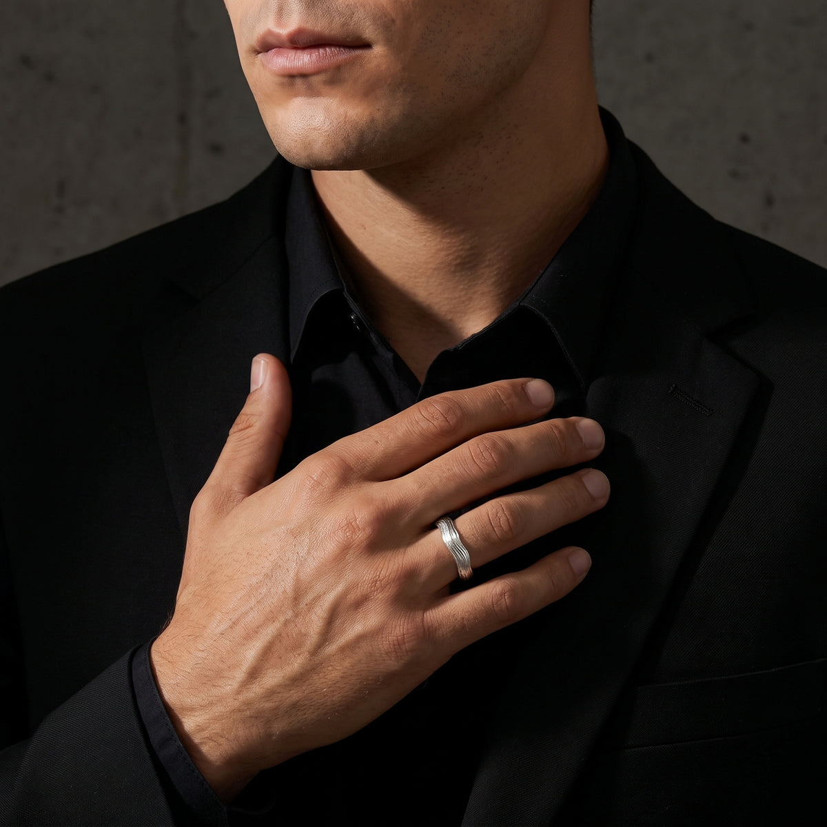 Man wearing the silver textured wave ring on his ring finger with his hand across a dark jacket.