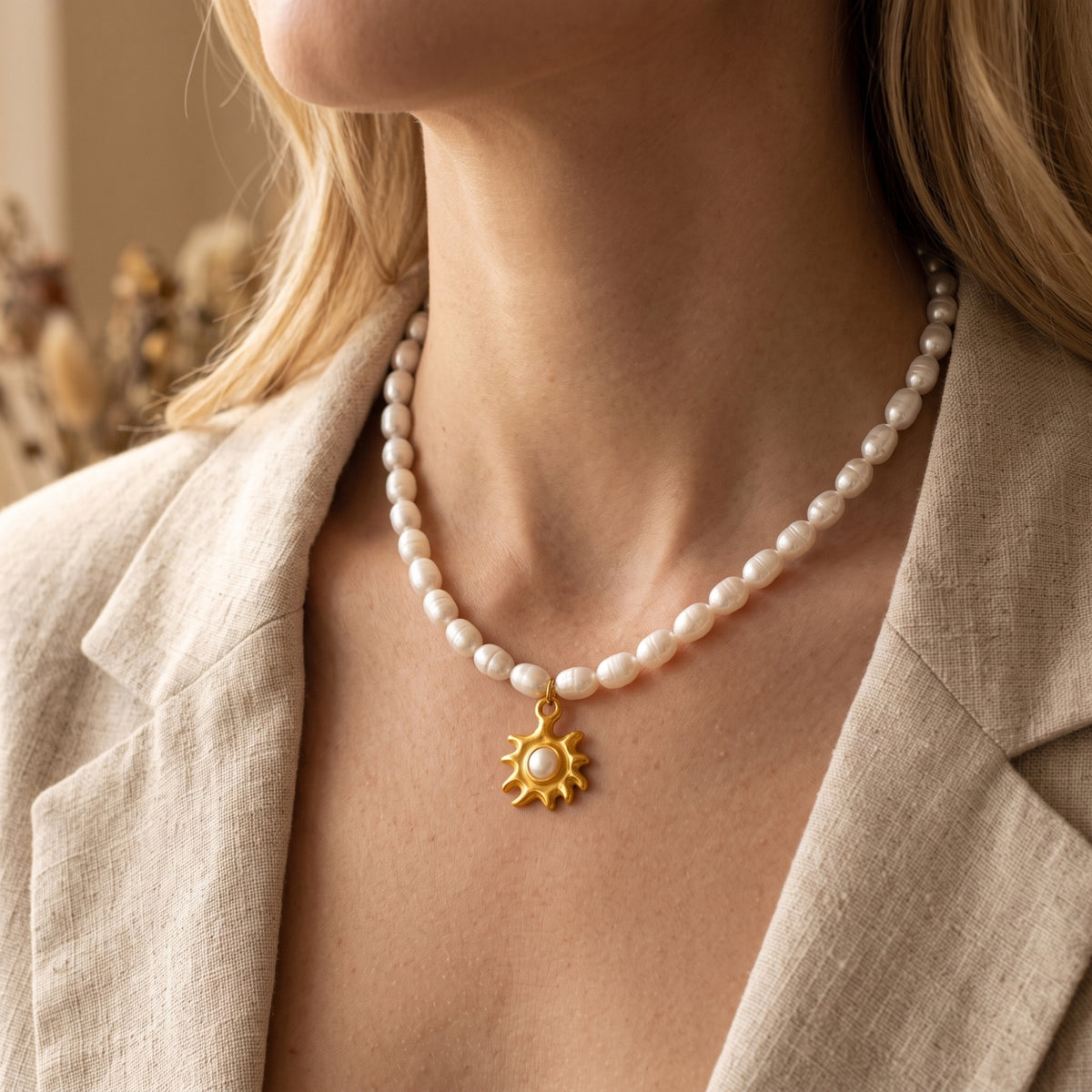 Solina pearl necklace with a gold sunburst pendant worn by a model in a beige linen blazer.