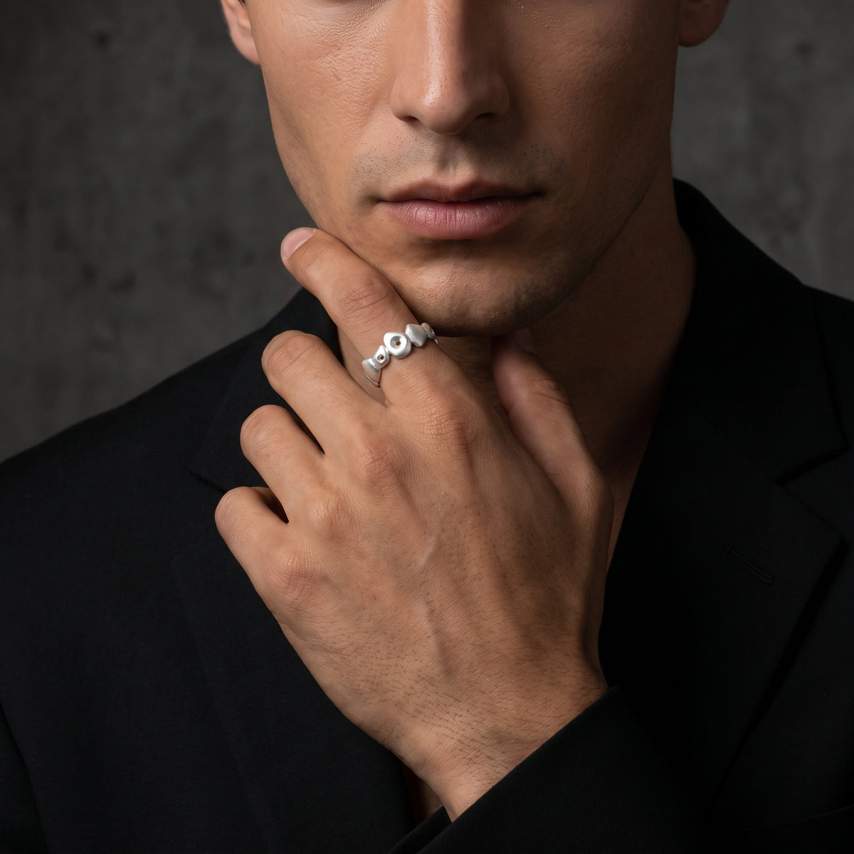 Man in a black blazer wearing the silver pebble open-band ring while touching his chin.