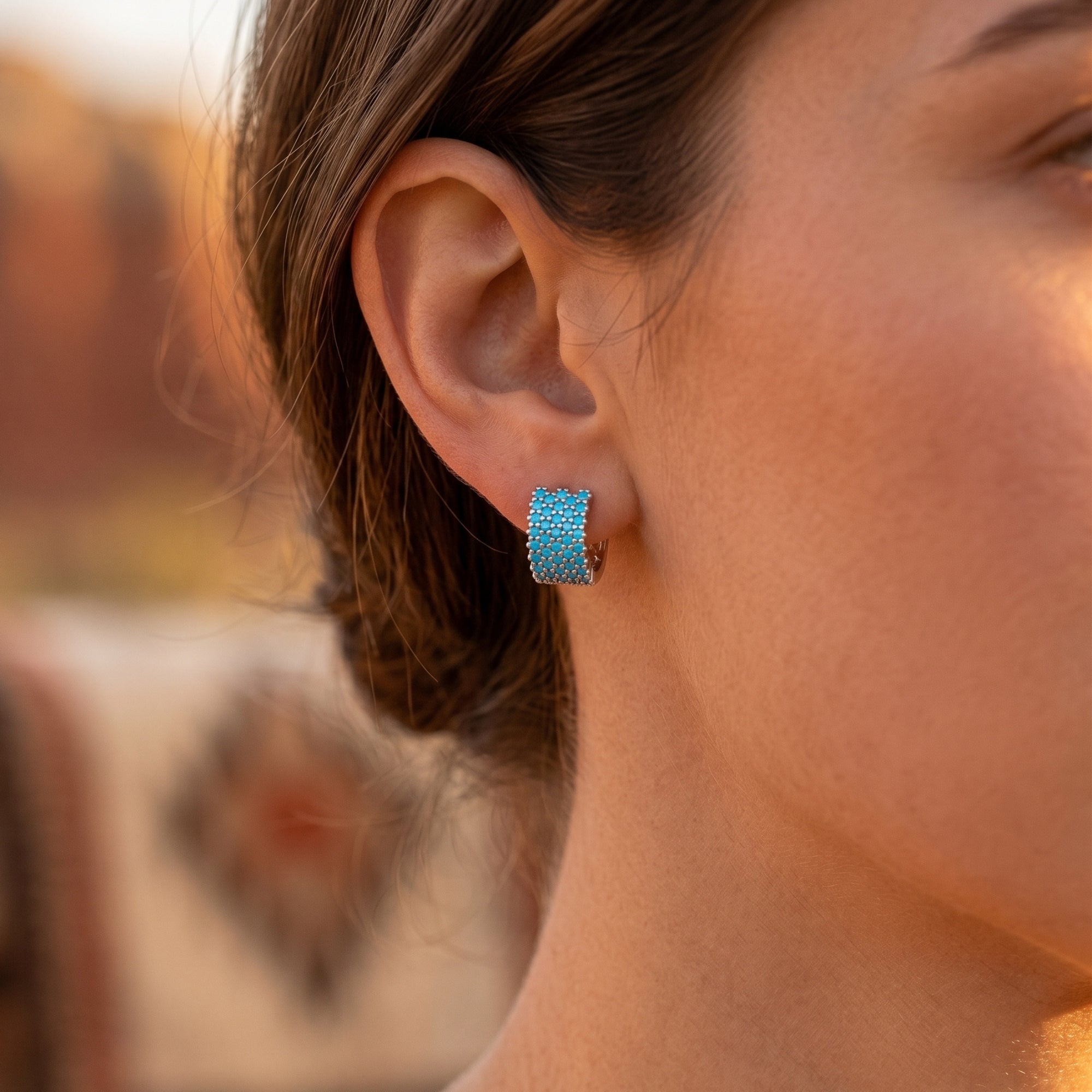 Side view of a model wearing a sterling silver turquoise huggie earring in a desert landscape.