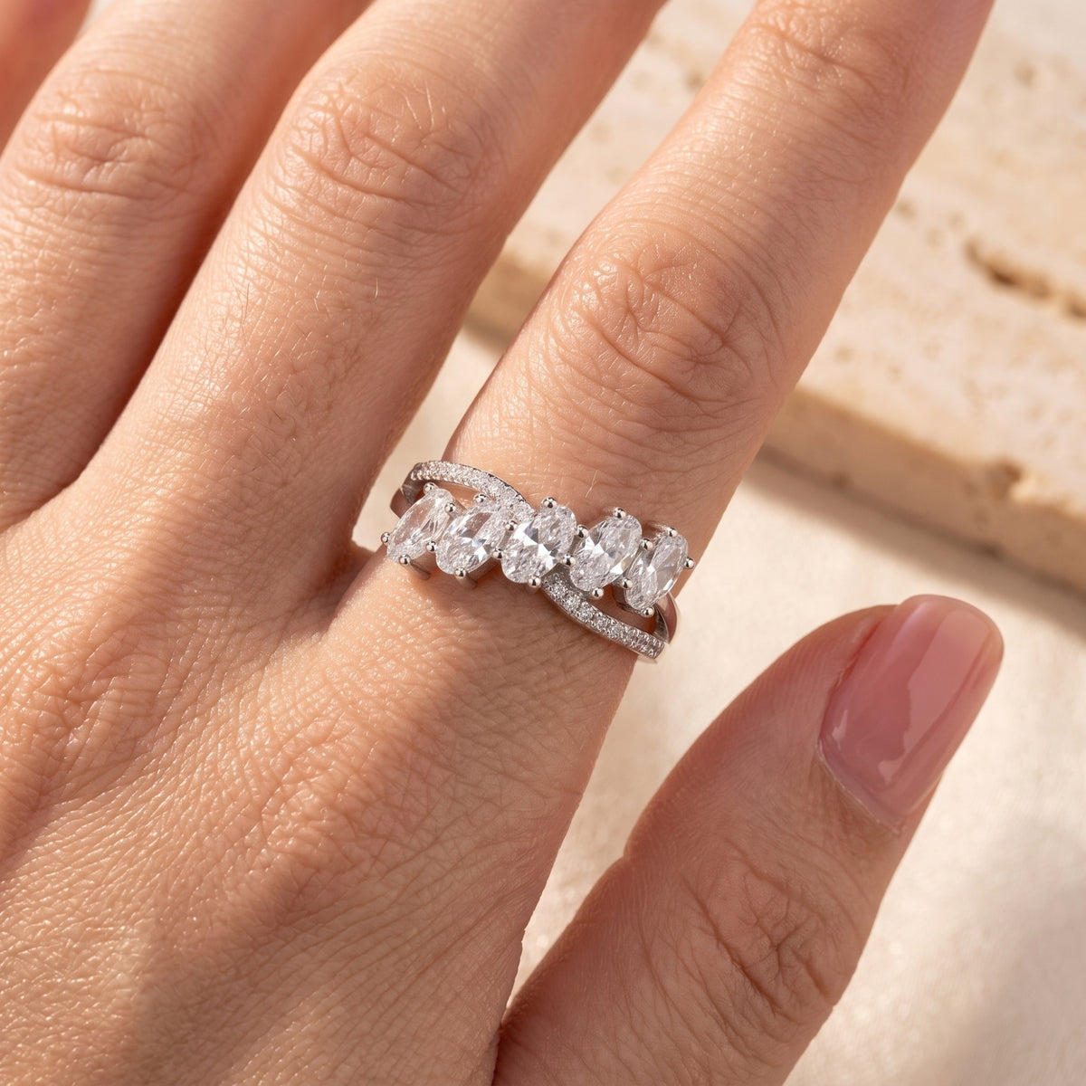 Hand model view of a five-stone oval cluster ring with pavé accents on the curved bypass band.