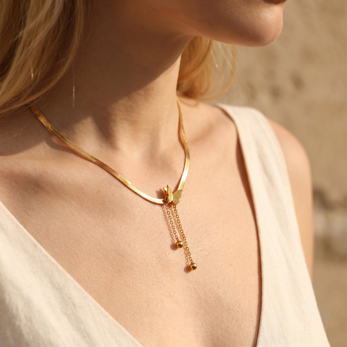 Angled view of a model wearing the gold-tone butterfly necklace resting flat against the collarbone.