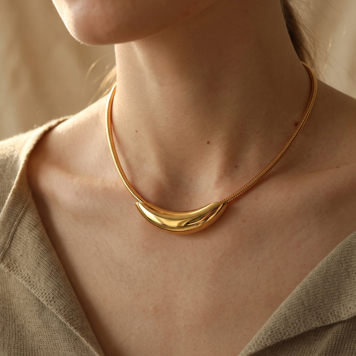 Close-up on-model view of the gold-tone curved crescent collar necklace worn with a knit top.