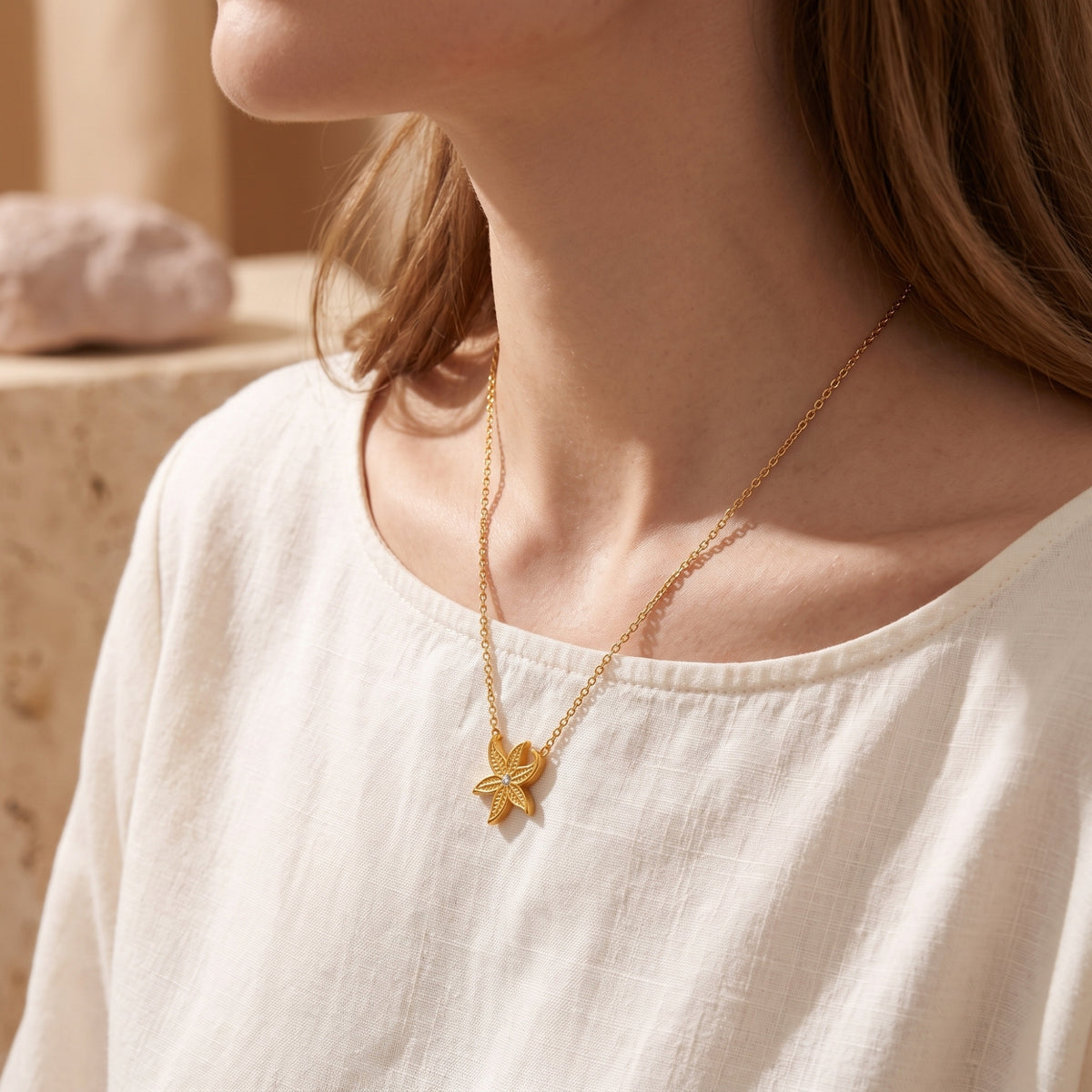 Woman wearing the gold starfish pendant necklace with a white linen shirt in a bright lifestyle setting.