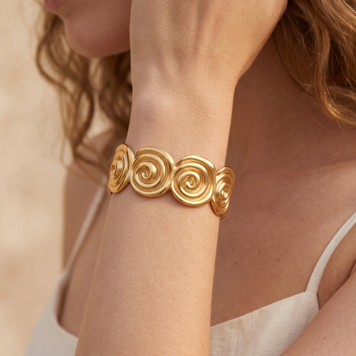 Model wearing the gold-tone spiral cuff bracelet on her wrist beside a white top, shown in a close-up portrait crop.