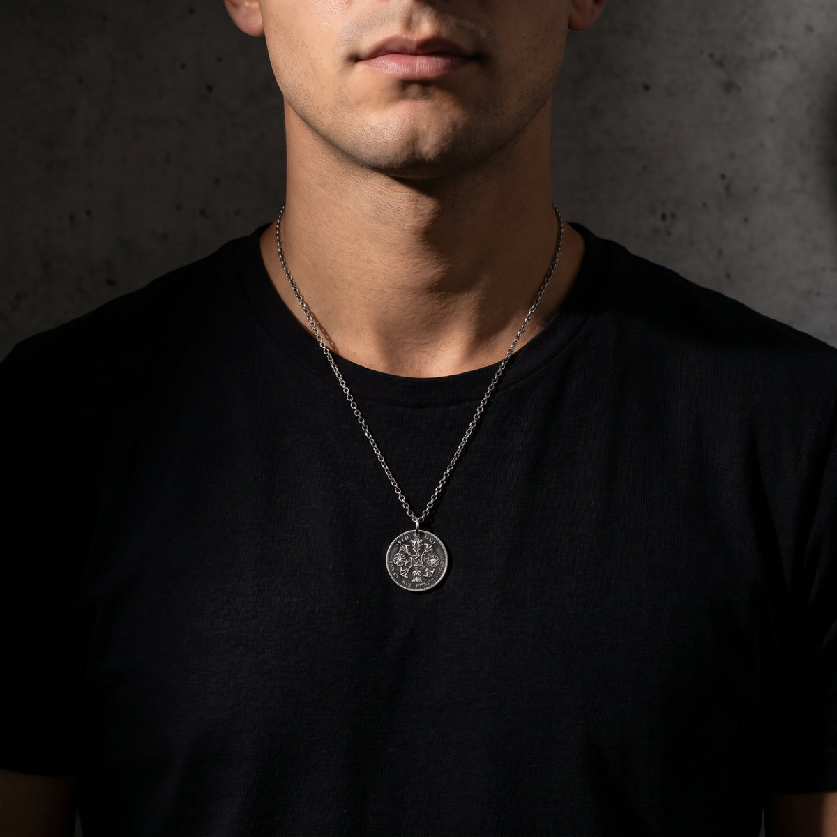 Frontal view of a man wearing the silver coin pendant necklace centered over a black crewneck shirt.