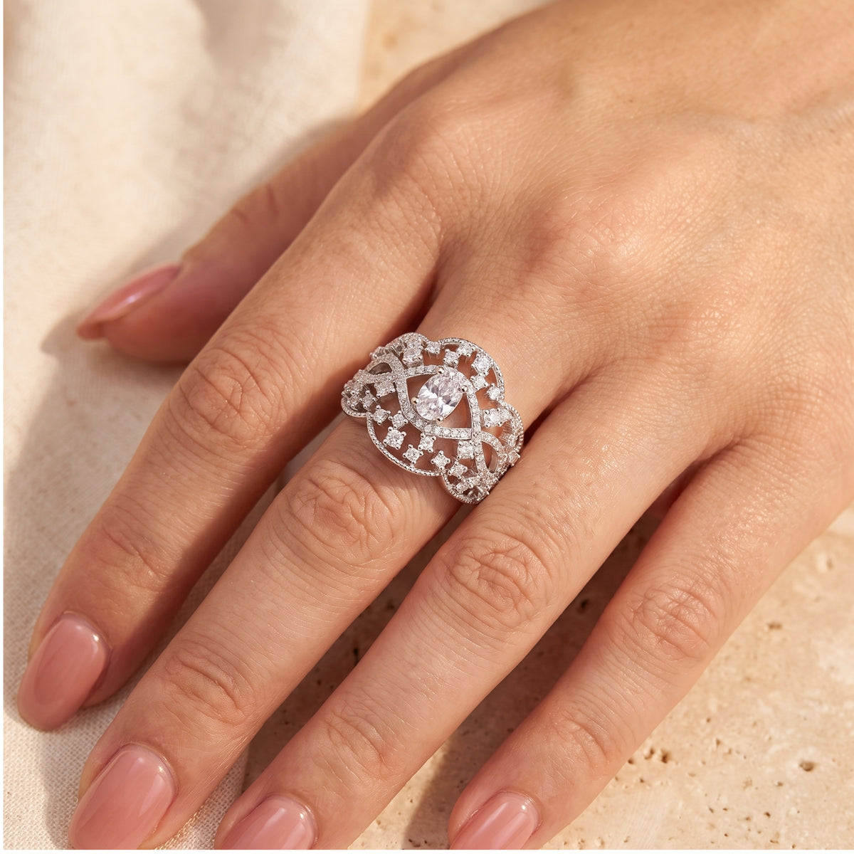 Overhead view of the wide silver lace ring worn on a hand against a warm neutral background.