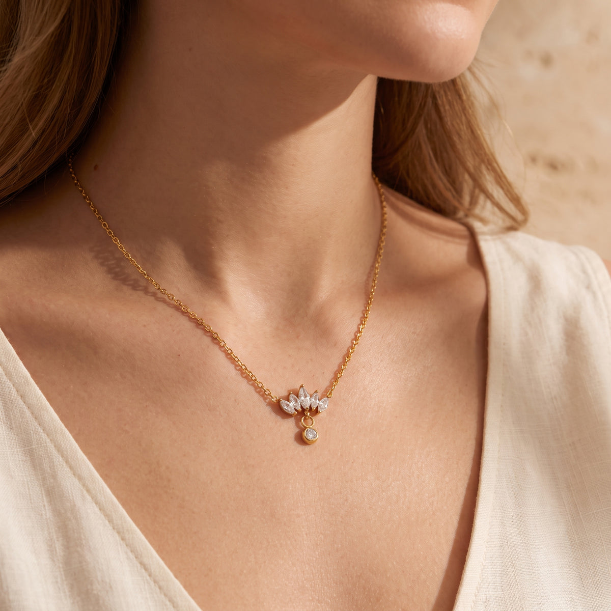 Wider model view showing the fit and drop of the gold-tone lotus marquise necklace on a light linen top.