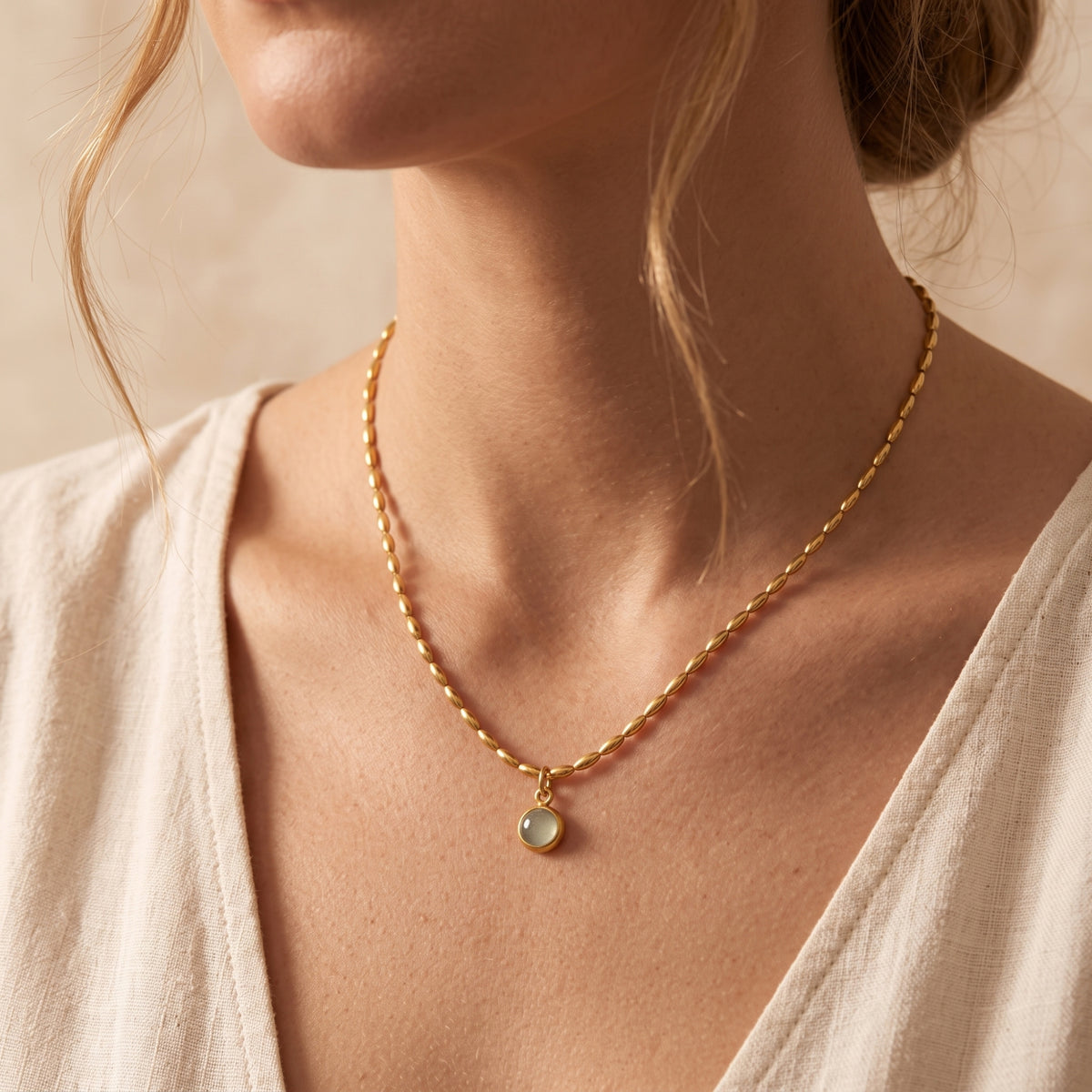 Front close-up of a model wearing the gold-tone oval-bead necklace with its round pendant on the upper chest.