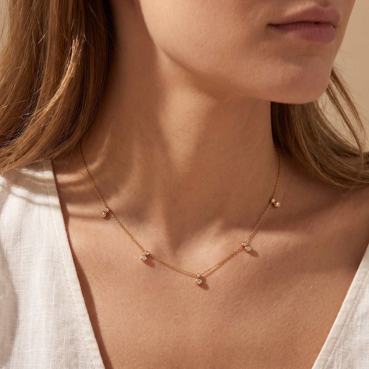 Front close-up of a model wearing the gold-tone station necklace with clear round bezel-set accents.