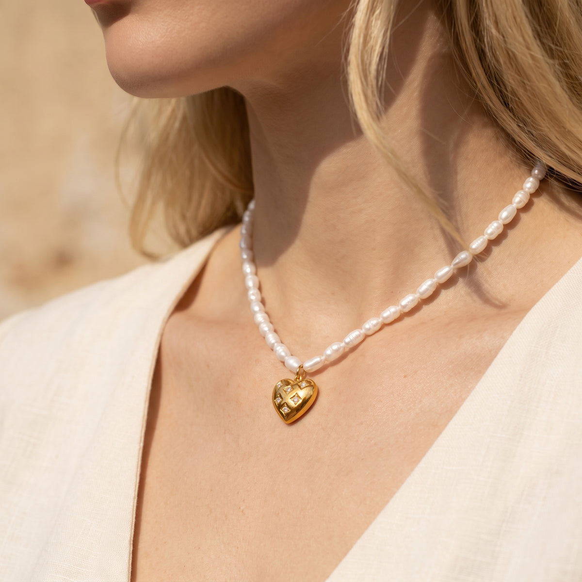 Three-quarter view of a model wearing the white pearl necklace with a gold-tone heart pendant.